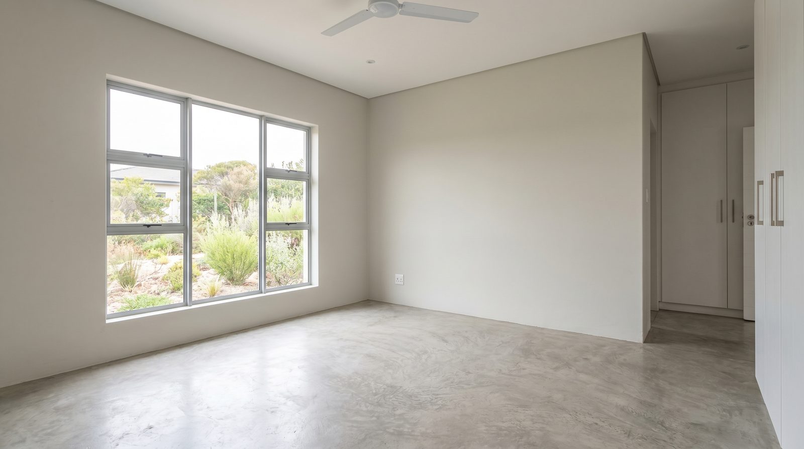 An empty main bedroom with bare floor and a window in a South African home